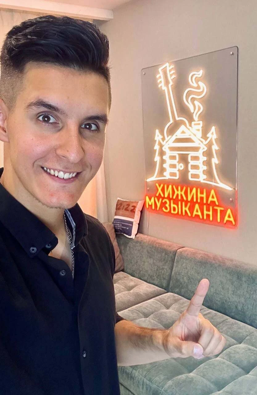 Мужчина рядом с неоновой композицией Хижина музыканта