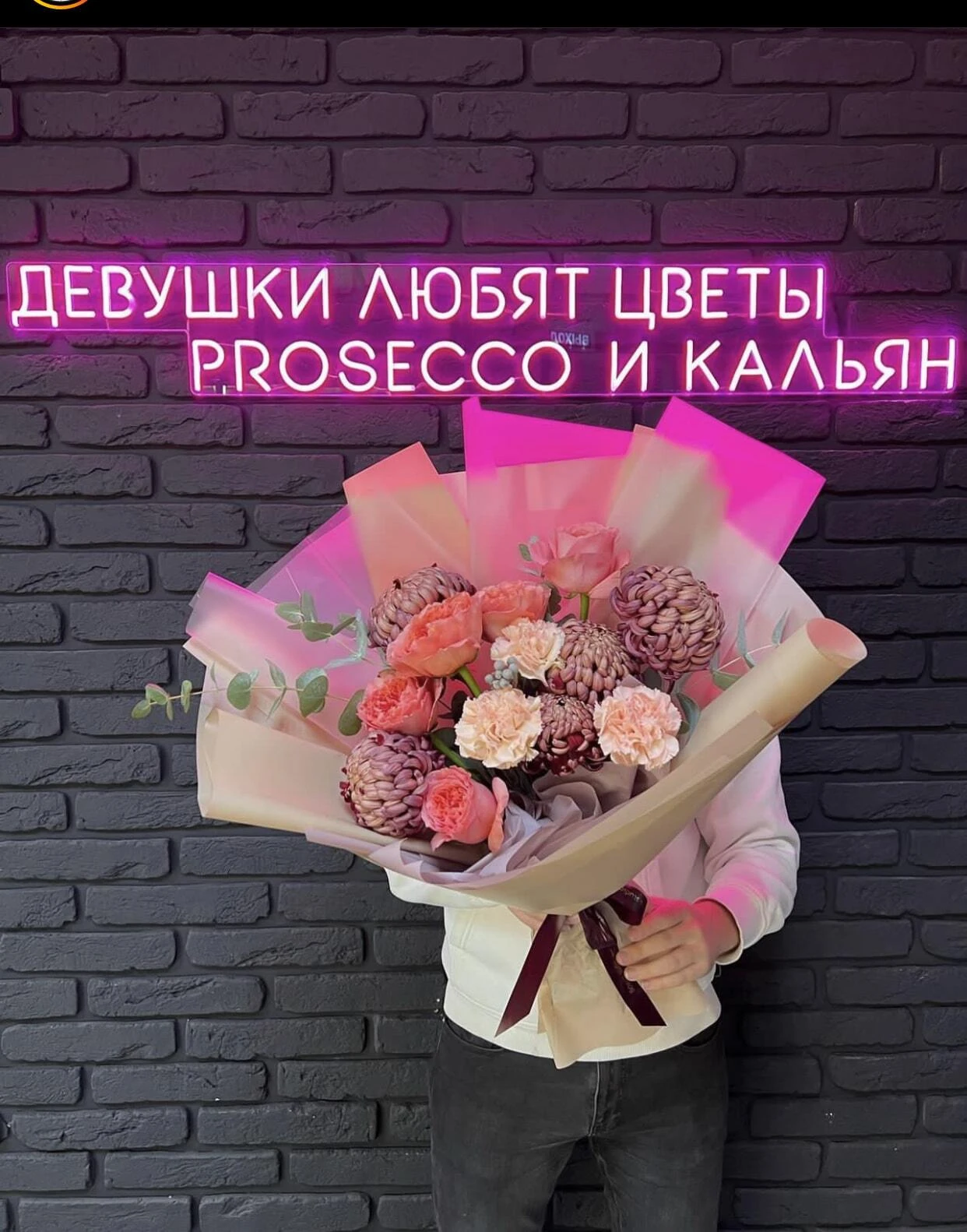 Розовая неоновая надпись над букетом цветов на кирпичной стене